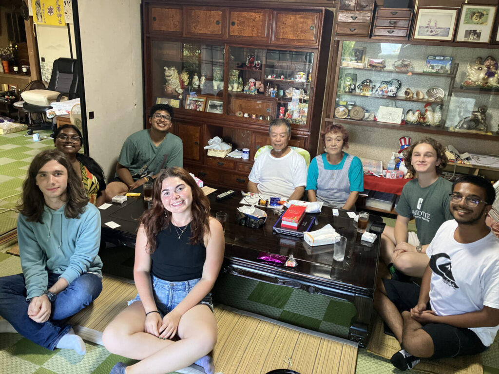 A smiling group of visitors and their local host family taking a commemorative photo in a traditional Japanese living room