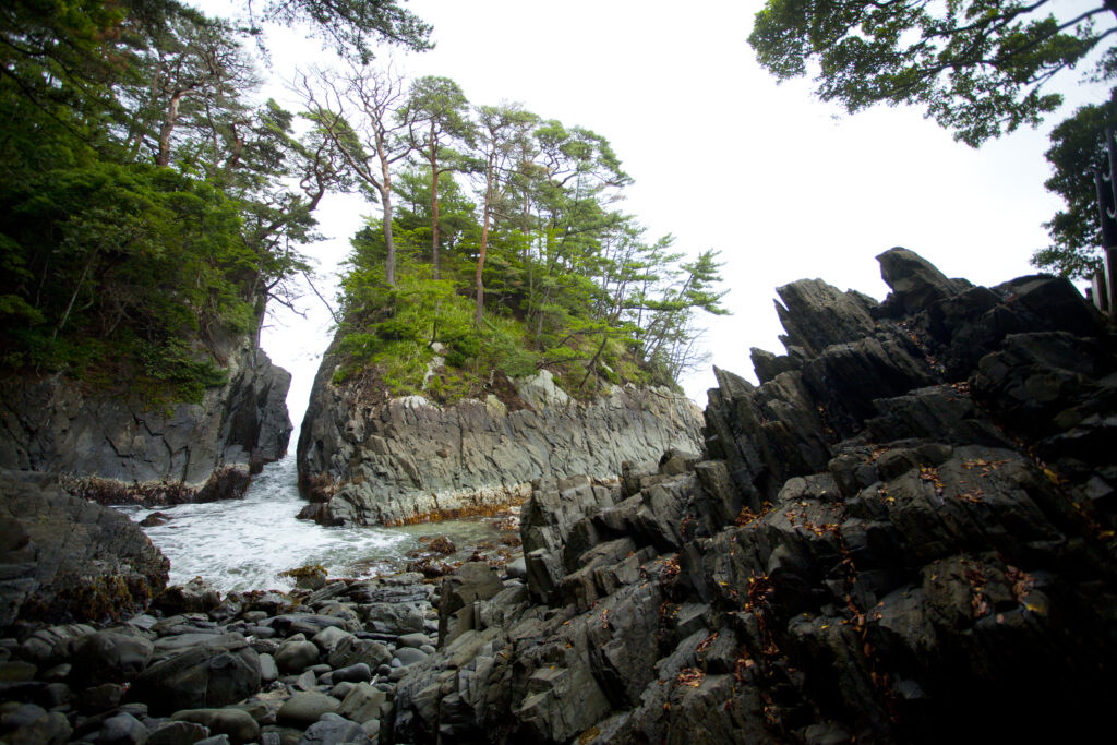A wide panoramic view of Cape Kamiwarisaki, showcasing the rugged cliffs and the powerful ocean waves of Minamisanriku