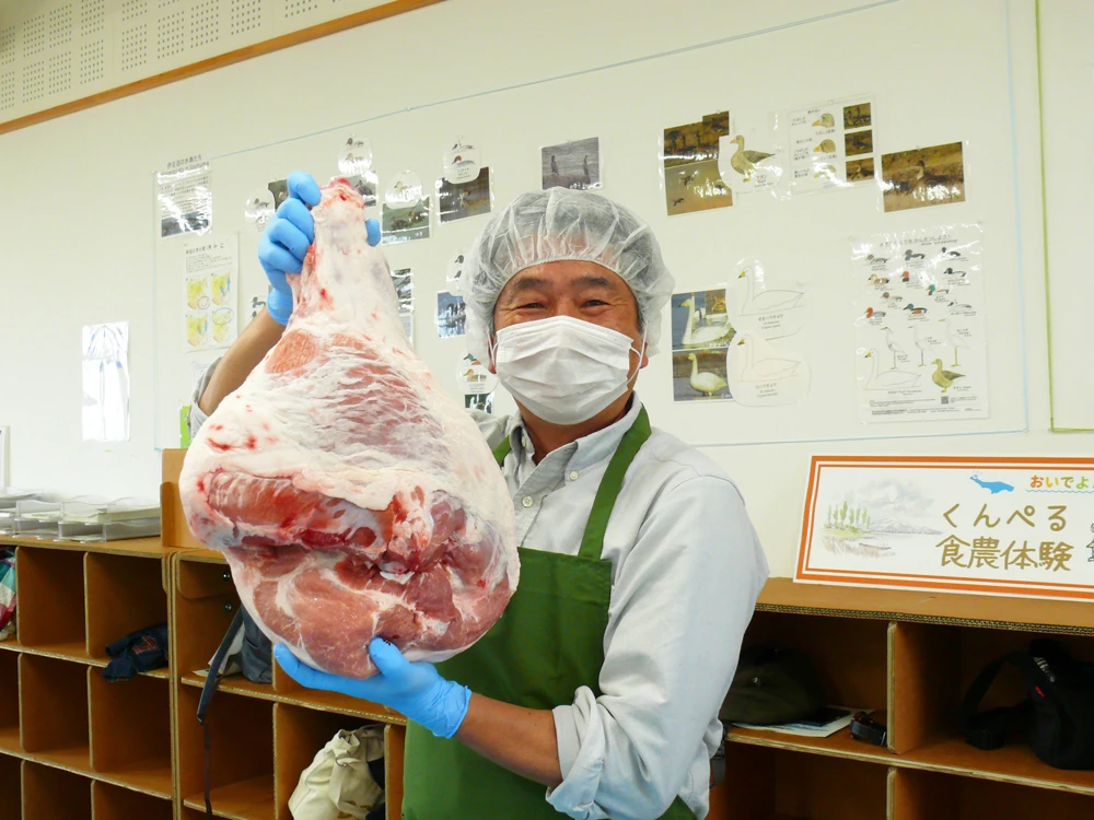 A fun commemorative photo of participants holding a massive block of high-quality pork before the meat processing workshop